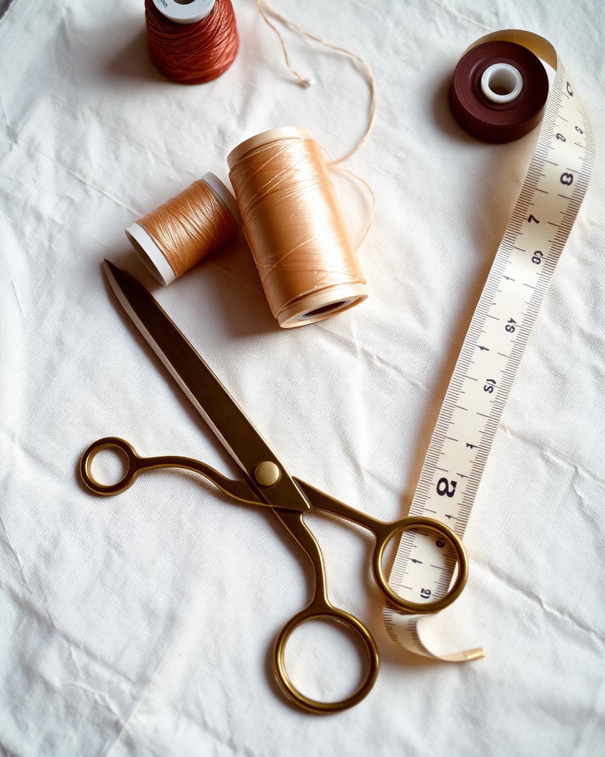 Gold tailoring shears, silk threads and a tape measure arranged on white linen